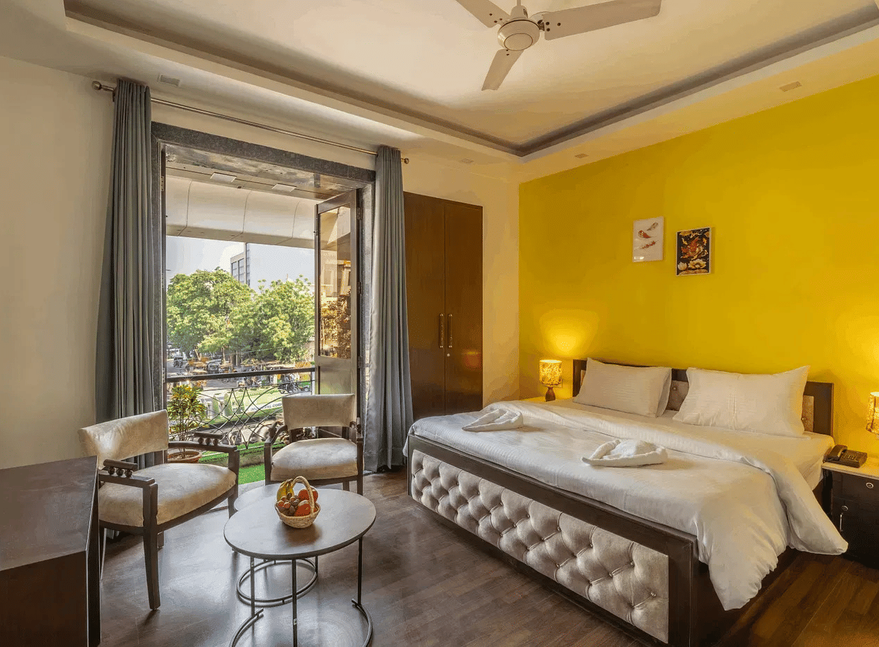 A hotel room with twin beds, yellow accents, and a view of greenery through the window - Lime Boutique Bed & Breakfast | Nehru Place Metro